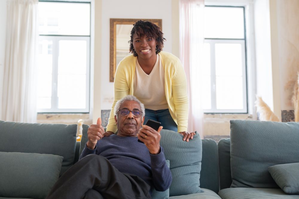 A caregiver and an older man laughing together on the sofa at home