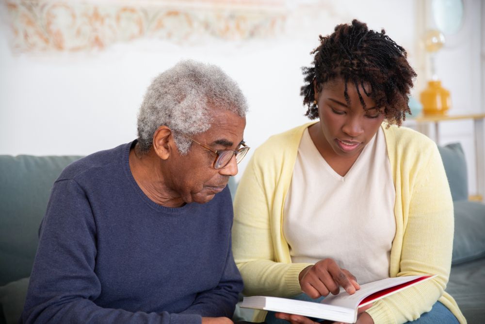 A caregiver reading a book together with an older man at home